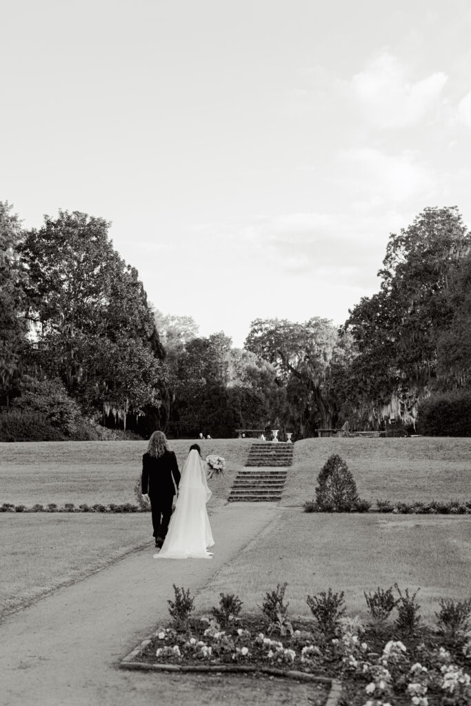 A bride beams with joy while holding a bouquet of pastel flowers, walking hand in hand with her groom as guests look on, smiling and clapping.