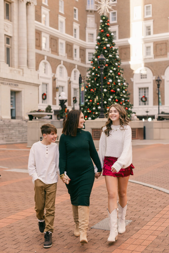 A mother and her two children walk hand in hand in front of a Christmas tree at a plaza in downtown Greenville SC. Dani Lacey Photographs