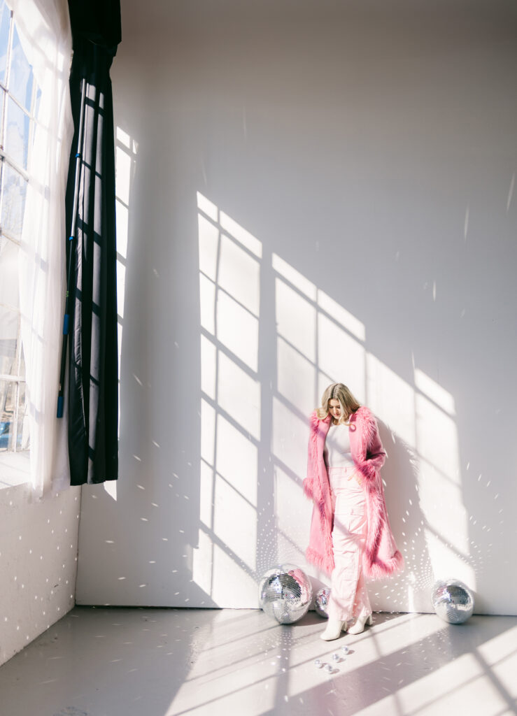 Editorial brand portrait of a woman in a hot pink fur coat surrounded by disco balls and window light in Greenville South Carolina by Dani Lacey Photographs.