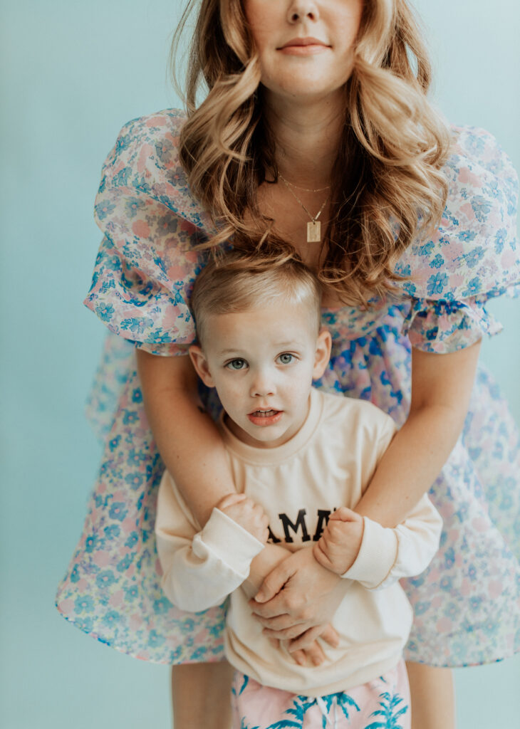 Mother and toddler son pose in studio with soft colors and floral textures.