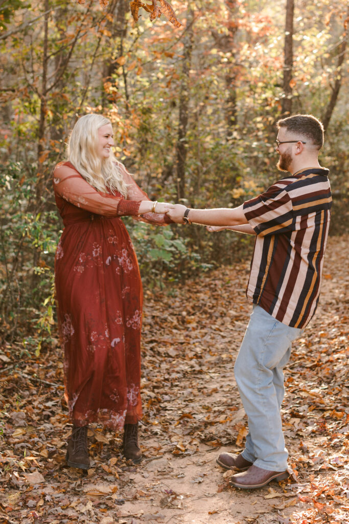 Engaged couple smiling and dancing in autumn leaves at Campbell’s Covered Bridge during fall engagement shoot. Dani Lacey Photographs.