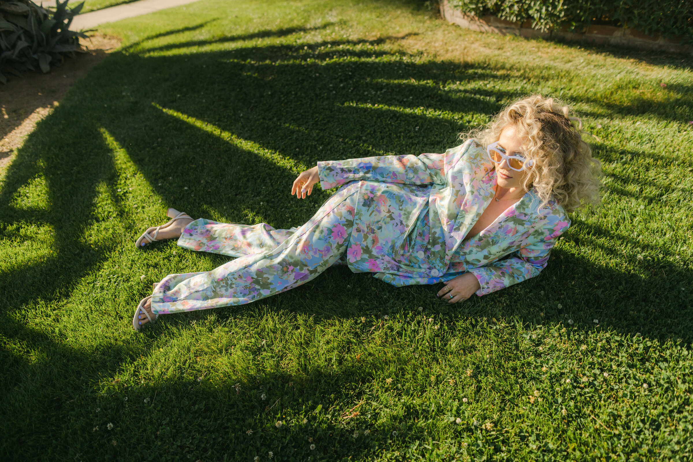 Confident female entrepreneur lying in the grass in a floral power suit during golden hour — a perfect visual to spark ideas on questions to ask your brand photographer before booking. Captured in Greenville, SC by Dani Lacey Photographs.