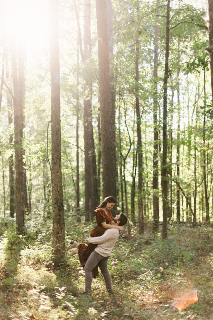 Man lifting his partner in a joyful embrace in the forest at Clemson Botanical Gardens. Easy photo spots in Greenville SC.