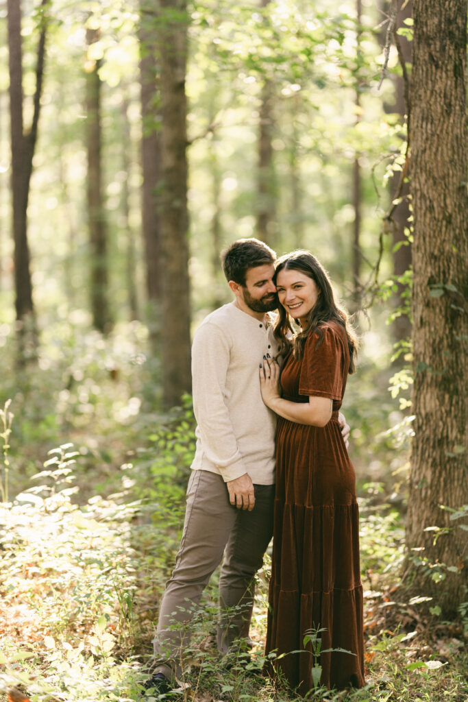 Smiling couple embracing in a forest clearing at Clemson Botanical Gardens