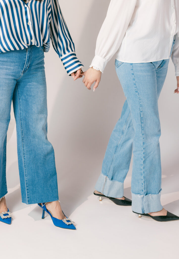 Two women wearing denim and button-up shirts holding hands during a modern studio branding session — a visual representation for questions to ask your brand photographer before booking.