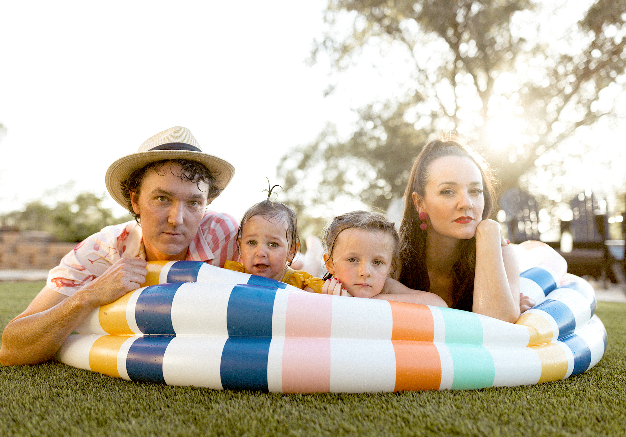 Family laying on the edge of a rainbow-striped inflatable pool at sunset – photographed in Greenville SC by Dani Lacey Photographs.