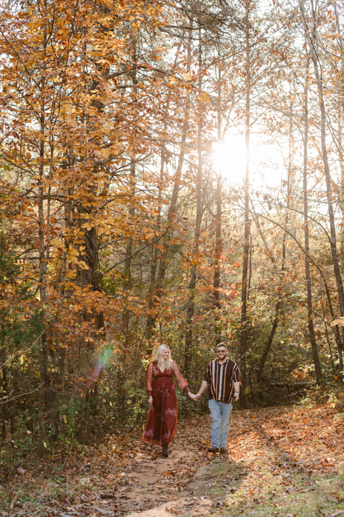 Couple walking hand in hand through the woods with glowing golden hour sun during fall engagement shoot in South Carolina. Dani Lacey Photographs.