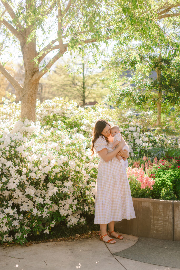 A mother holds her baby surrounded by blooming azaleas and spring florals at Falls Park in Greenville SC.