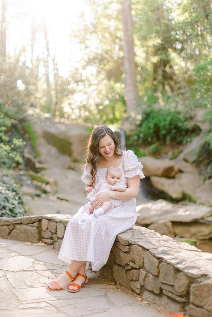 A mother sits with her baby on a stone wall in front of a waterfall at Falls Park in Greenville.
