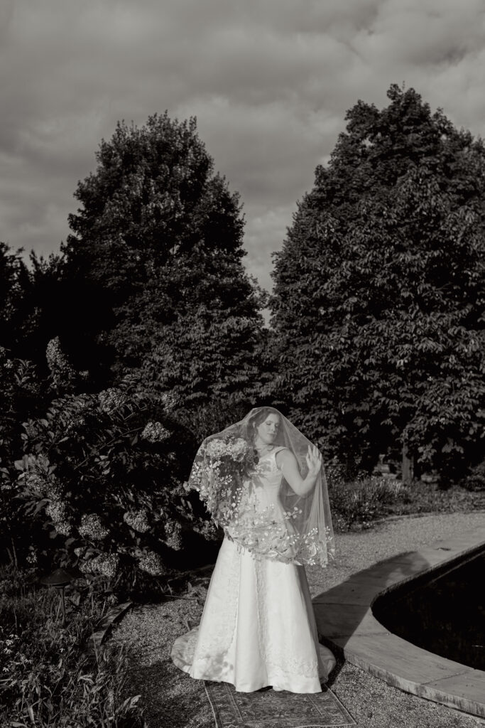 Black and white photo of bride in a garden holding her veil over her face at Furman University.