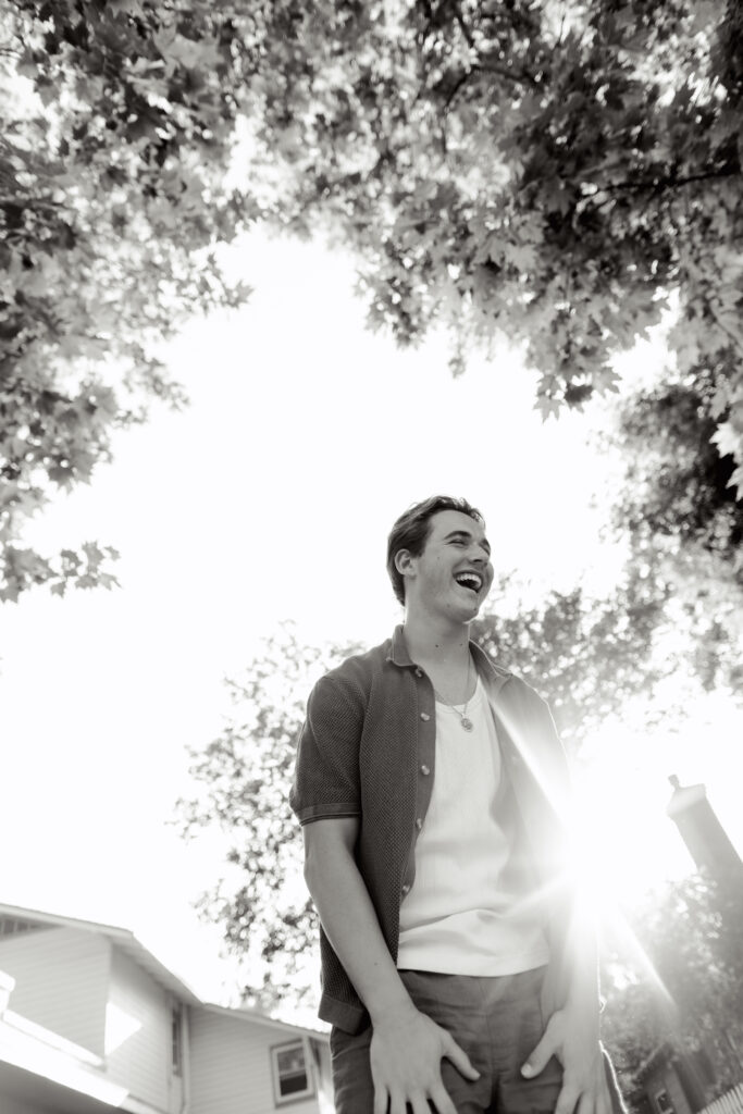 Teen boy laughing in a sunlit black and white photo under a canopy of trees.