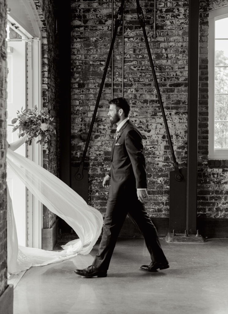 A groom walking toward his bride as her veil blows across the floor in a dramatic motion — a curated, cinematic frame captured in Greenville, SC by Dani Lacey Photographs.