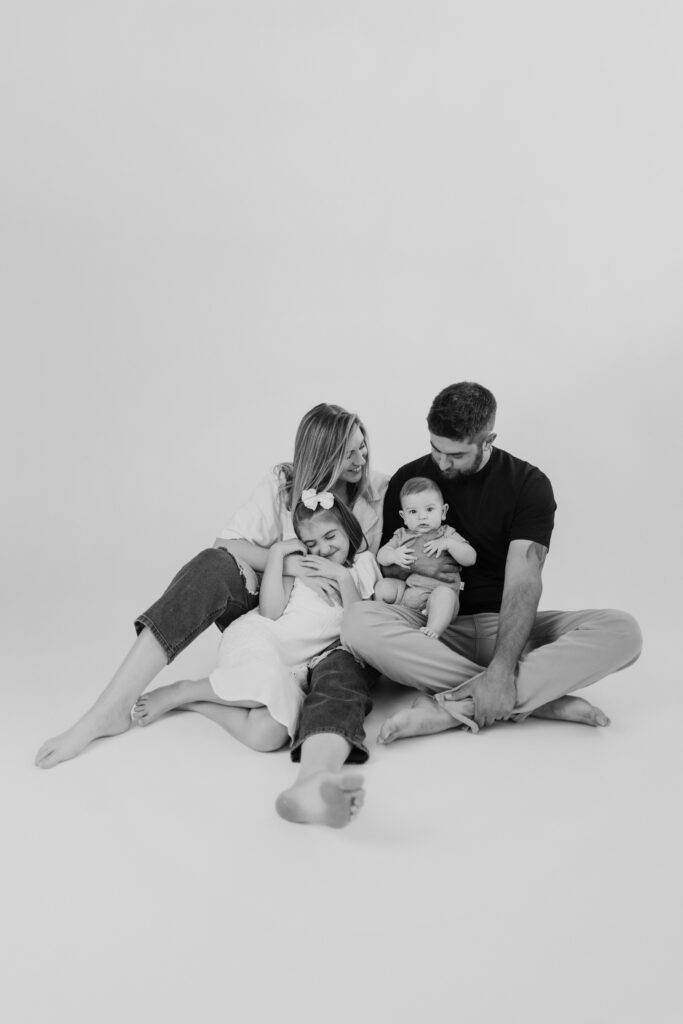 A relaxed, intimate black and white family portrait on a white studio floor, showcasing connection and comfort during a mini photo session in Greenville SC.