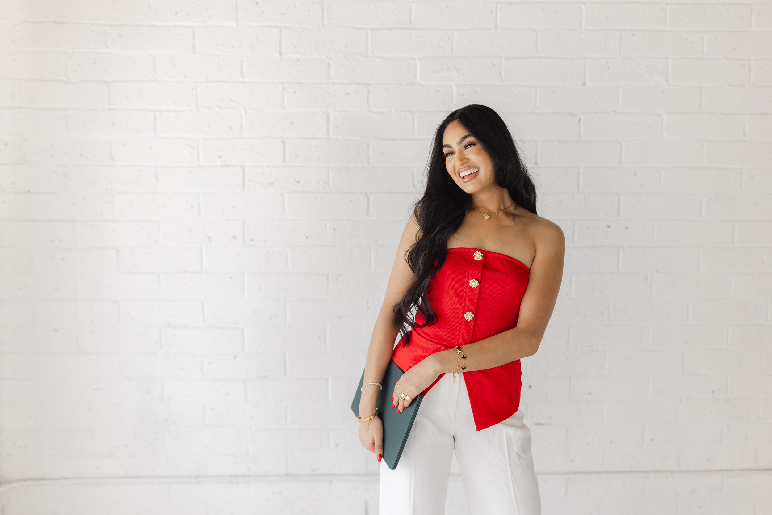 Confident female entrepreneur in red strapless top and white trousers holding a laptop during a modern branding photo session in Greenville, South Carolina – Dani Lacey Photographs