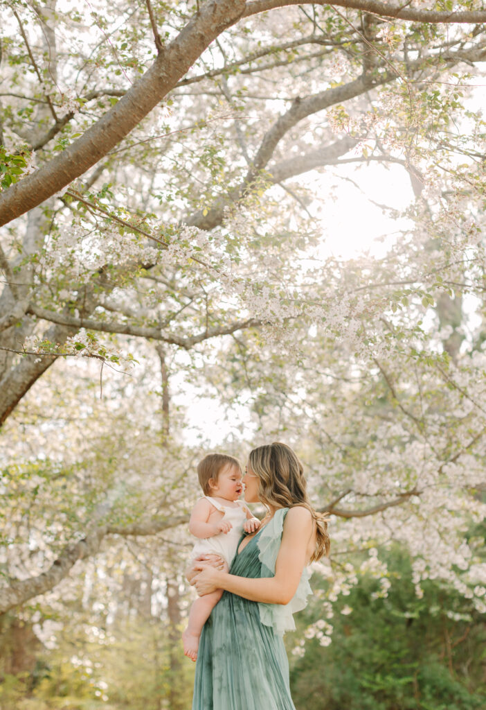 Mother holding baby under cherry blossom trees at Furman University during golden hour.
