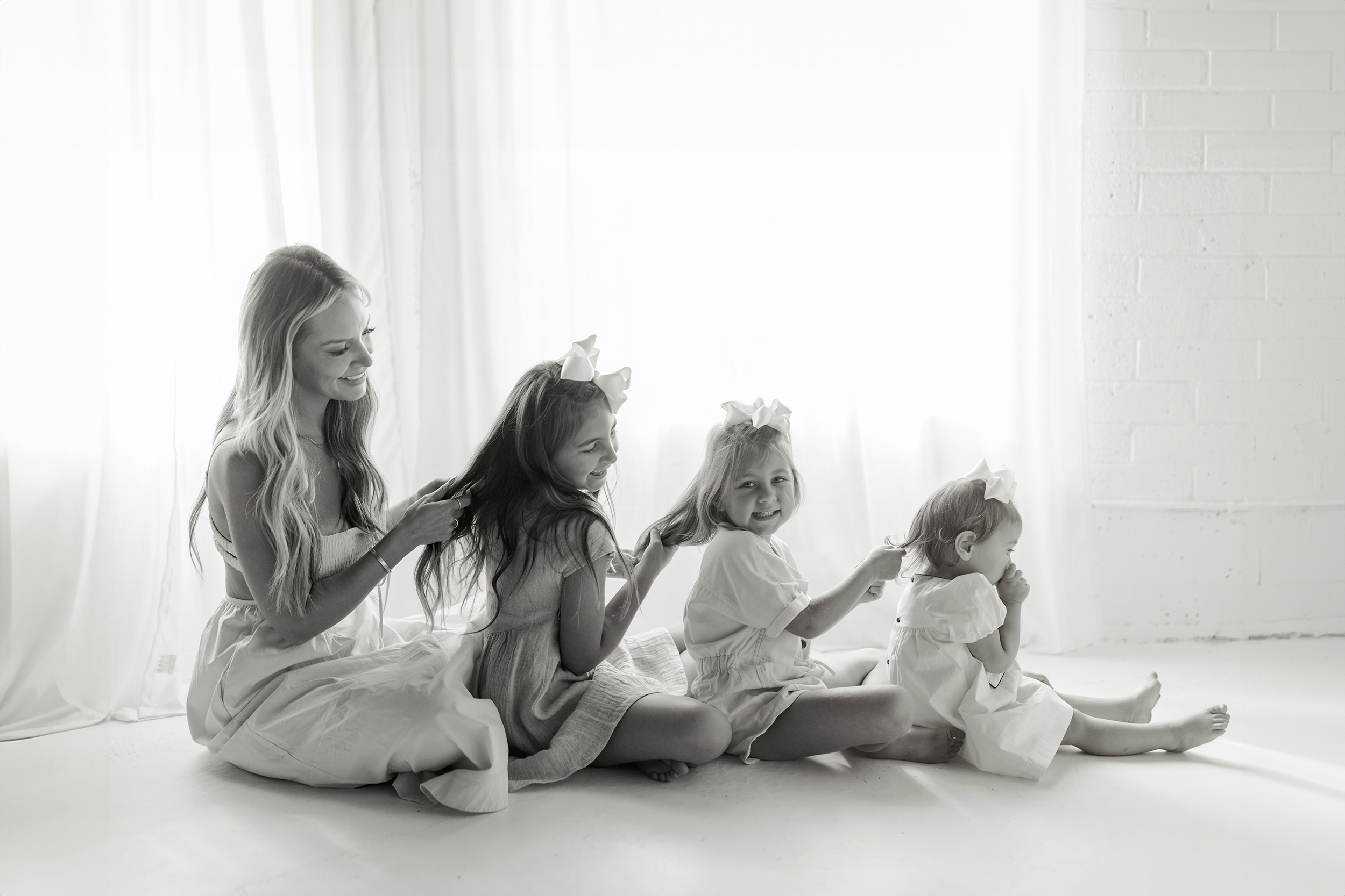 Mother and daughters sitting in a line, braiding hair during a studio family mini session in Greenville, South Carolina – Dani Lacey Photographs.