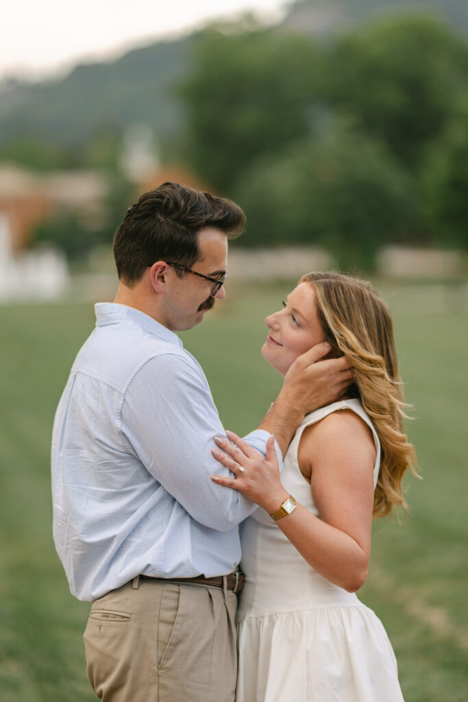 Man gently holds woman's face as they gaze at each other in an open field during golden hour.