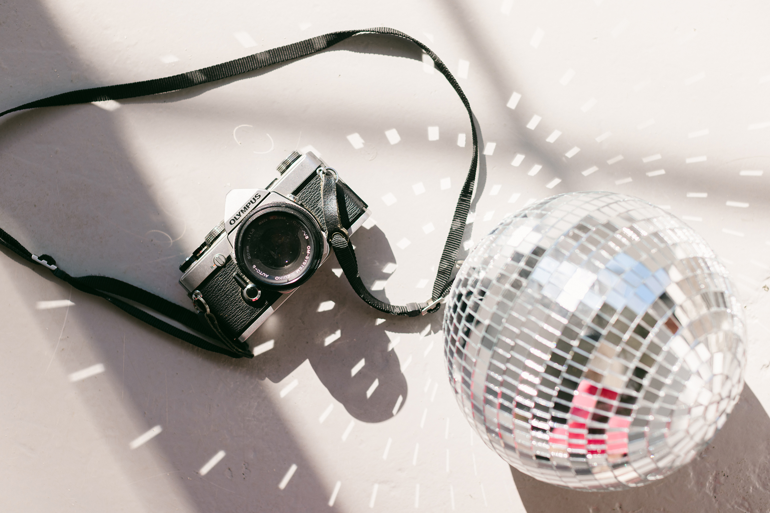 visually rebrand your business Flat lay of a vintage Olympus film camera beside a reflective disco ball, casting light patterns on a white floor