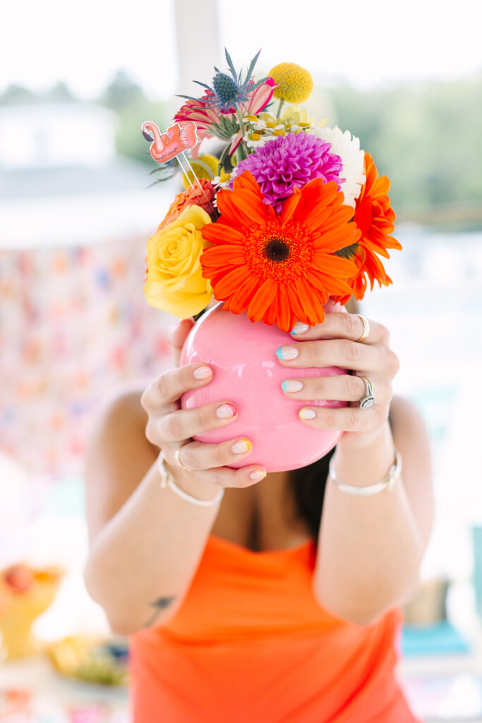 Close-up of woman holding pink vase with bold orange and yellow flowers, colorful nails on display — Pool Party Style Inspiration by Dani Lacey Photographs.