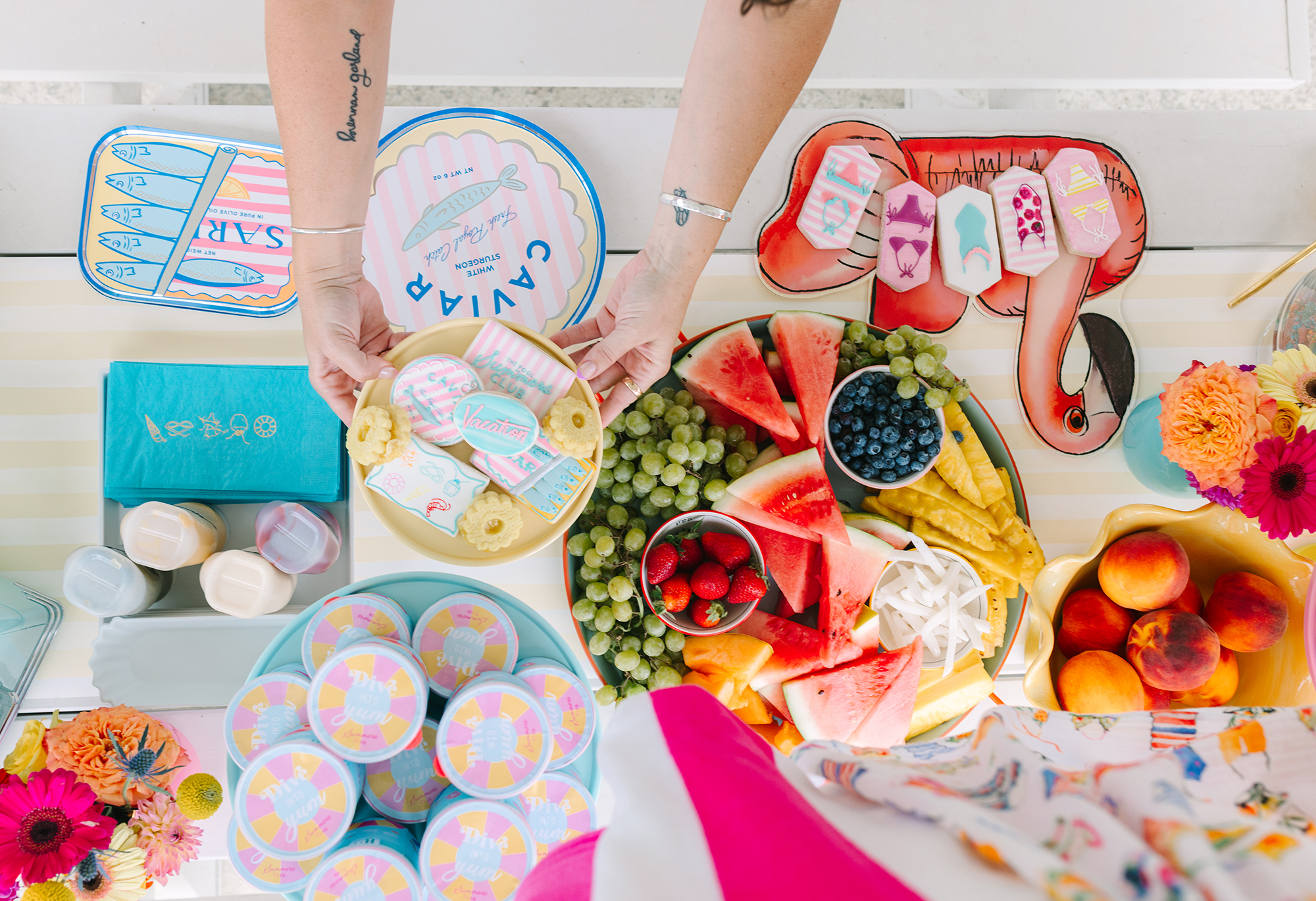 Flat lay of colorful pool party table setup with tropical fruit, playful cookies, and bold colors for summer birthday — Pool Party Style Inspiration by Dani Lacey Photographs.