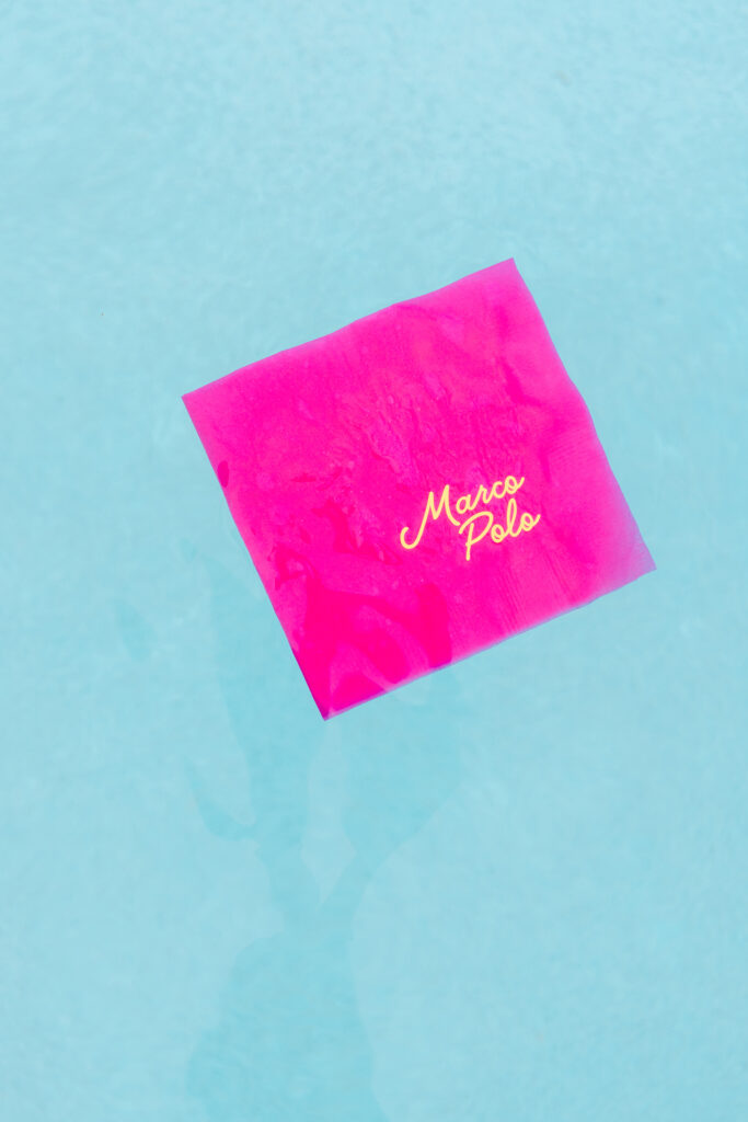 Vibrant pink “Marco Polo” napkin floating in aqua water for a fun and unique poolside detail — Pool Party Style Inspiration by Dani Lacey Photographs.