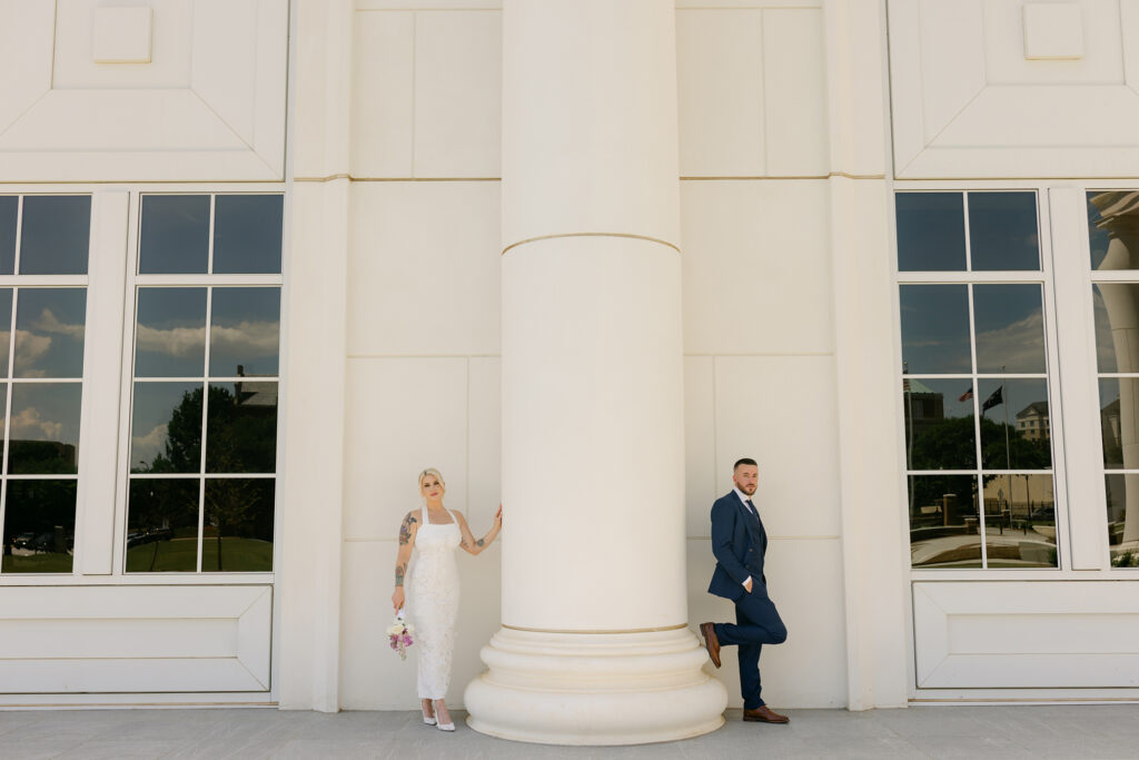 Bride and groom pose on opposite sides of a tall white column outside a modern courthouse building in Greenville, South Carolina. Captured by Greenville SC wedding photographer Dani Lacey Photographs.