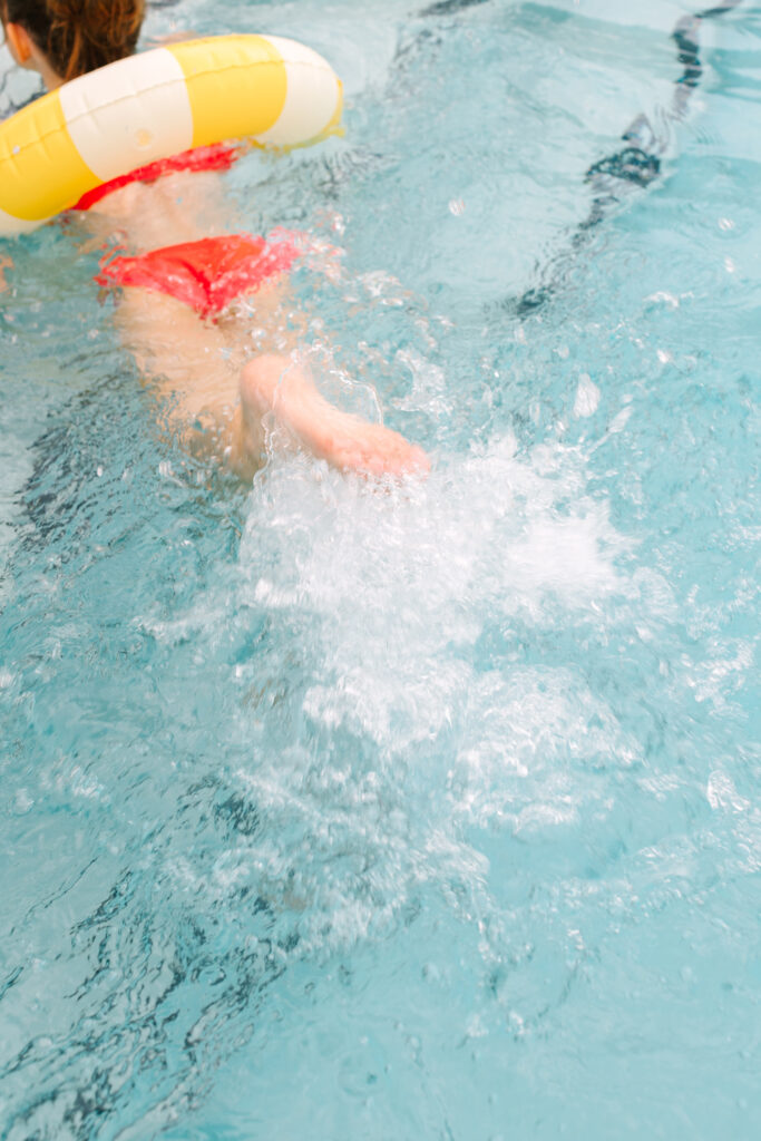 Playful summer moment of a girl swimming with a yellow and white floaty, captured in editorial style. Dani Lacey Photographs