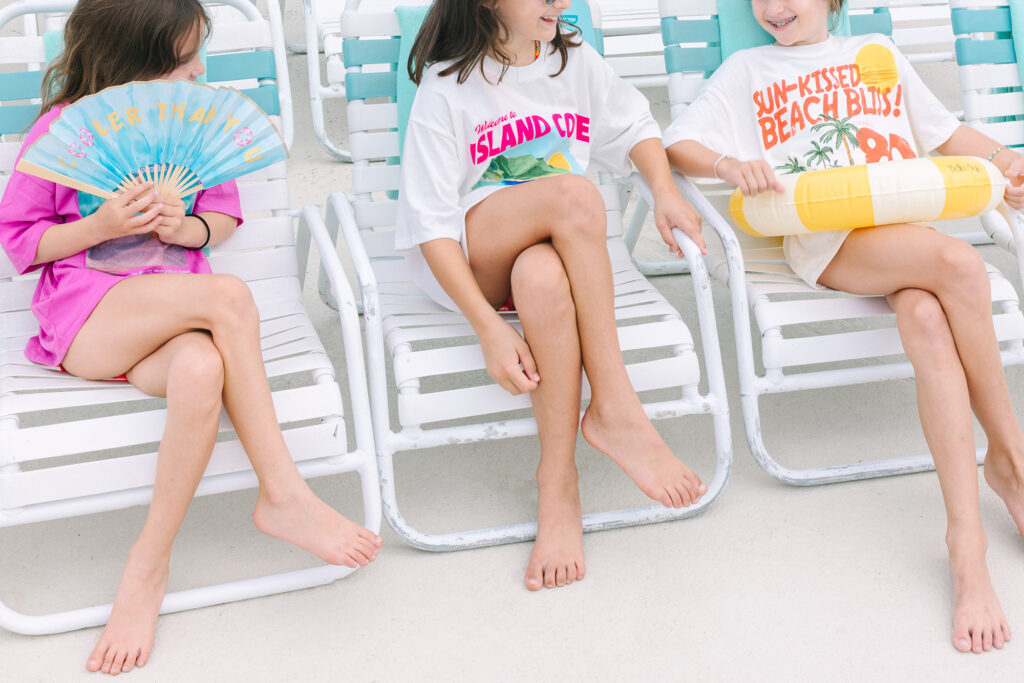Three girls lounging poolside in colorful retro tees with playful pool party graphics, capturing a stylish kids’ summer birthday. Dani Lacey Photographs