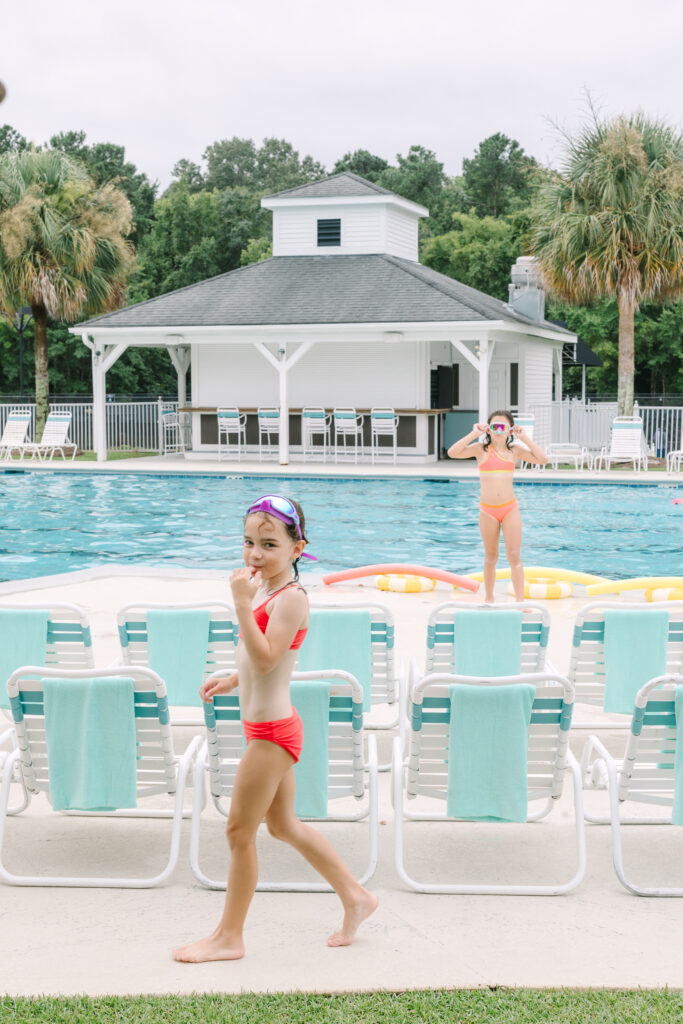 Two girls in red swimsuits playing near the pool with goggles during a summer birthday party. Captured by Dani Lacey Photographs.
