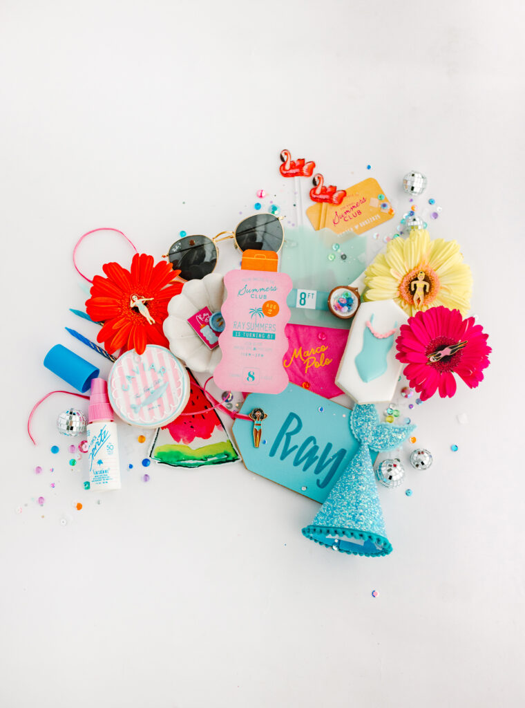 Colorful flat lay of pool party decorations including flowers, cookies, sunglasses, disco balls, and themed invitation for Ray Summers’ 8th birthday