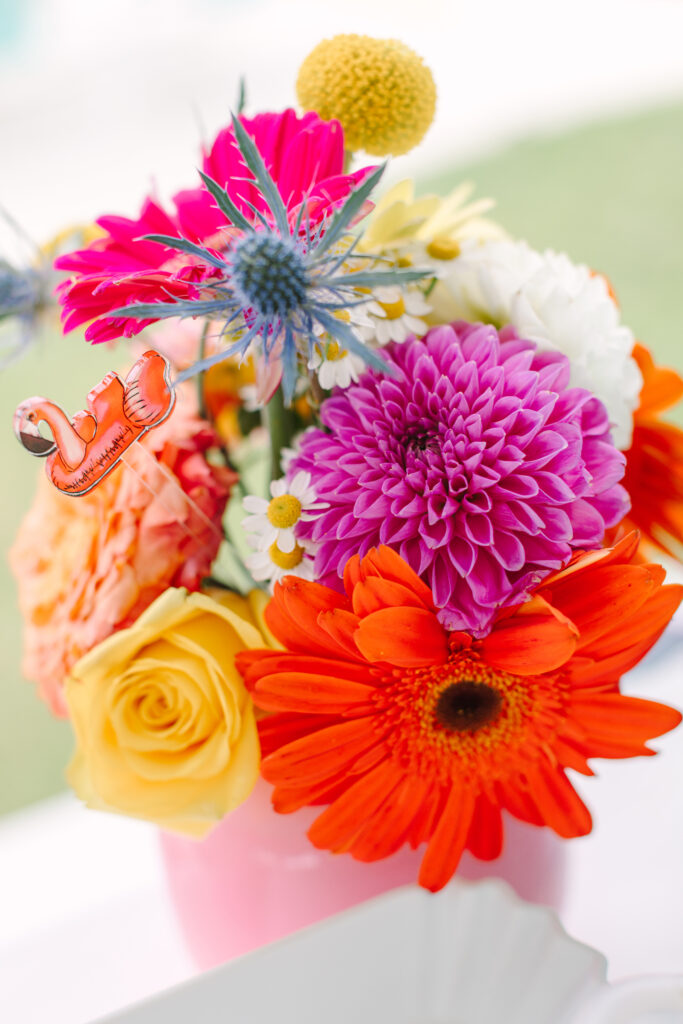 Close-up of a vibrant summer floral arrangement with pink, yellow, and orange flowers in a bright pink vase. Dani Lacey Photographs.