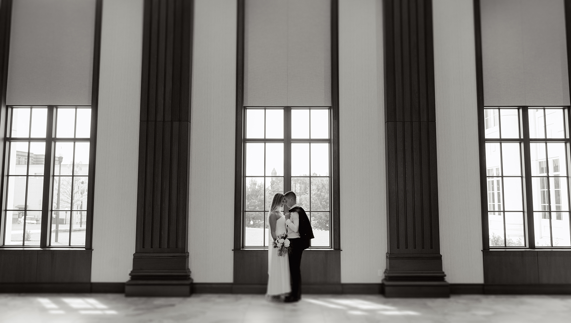 Bride and groom standing close together in front of a large window inside the Spartanburg County Courthouse, framed by tall columns, photographed by Greenville SC wedding photographer Dani Lacey Photographs.