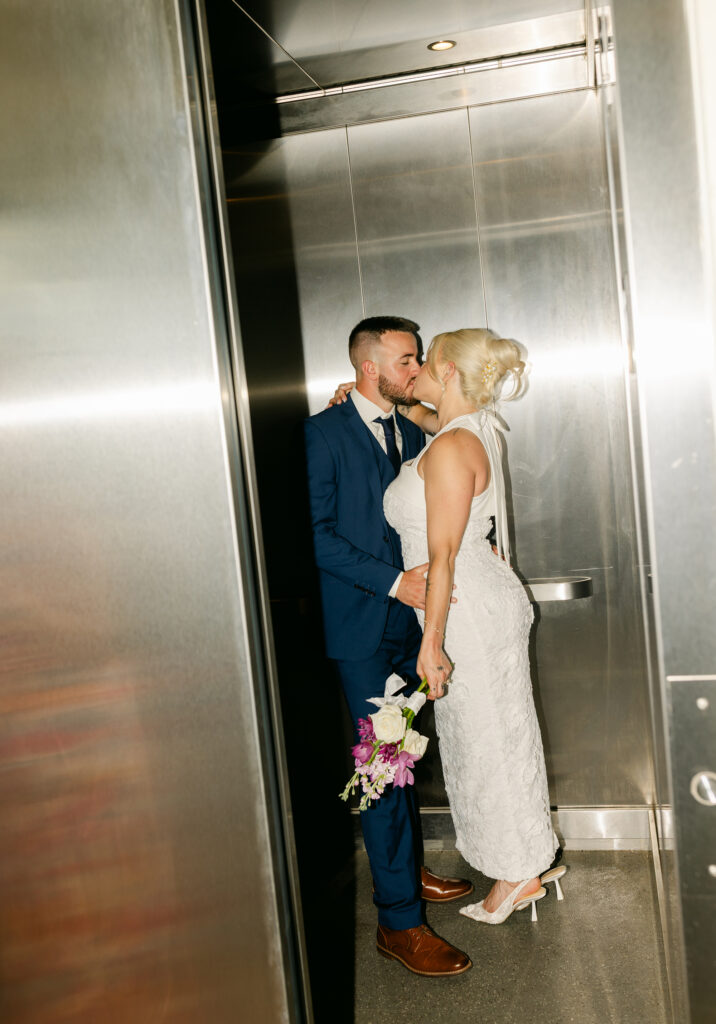 Bride and groom share a kiss inside a modern elevator at the Spartanburg County Courthouse, captured in a candid editorial style. Photography by Greenville SC wedding photographer Dani Lacey Photographs.