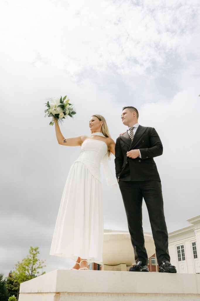 Bride raises her bouquet into the sky while standing beside the groom at the Spartanburg County Courthouse, captured in a modern editorial style. Captured by Greenville South Carolina wedding photographer Dani Lacey Photographs.