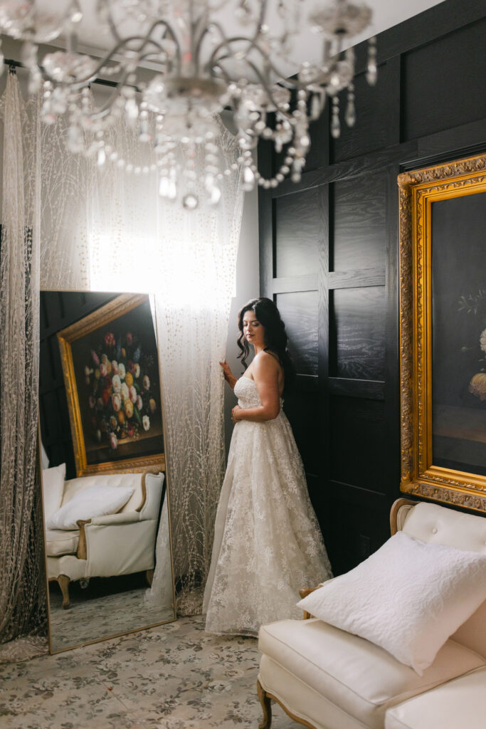 Bridal portrait at Edinburgh West in Greenville, SC, featuring bride in lace gown standing by a mirror with chandelier and vintage décor – Dani Lacey Photographs