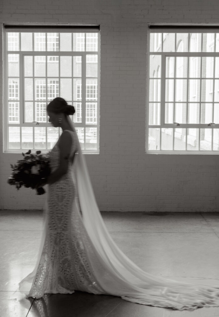 Black and white artistic silhouette of the bride walking with bouquet inside Judson Mill’s industrial windows.