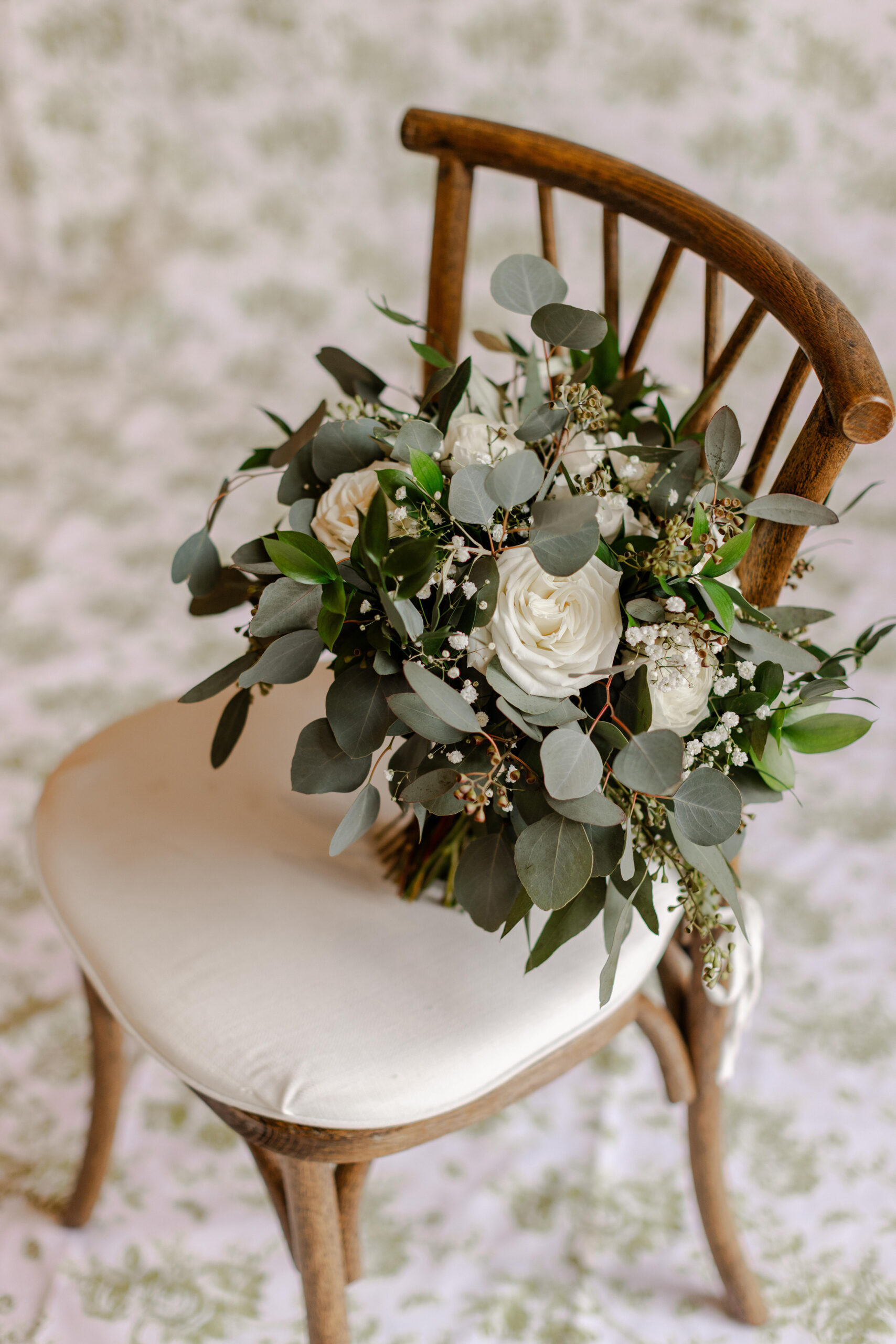 Elegant bridal bouquet with white roses, eucalyptus, and greenery styled on a wooden chair, photographed by Greenville wedding photographer Dani Lacey Photographs.