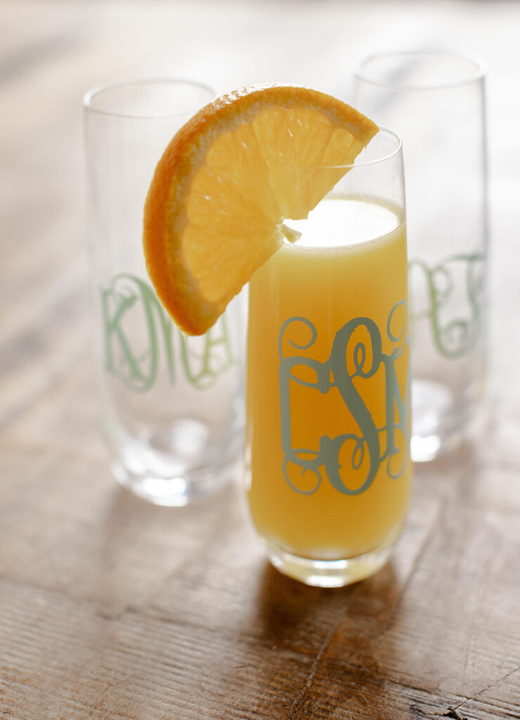 Close-up of a personalized mimosa glass with an orange garnish during bridal suite celebrations at Judson Mill, documented by Greenville wedding photographer Dani Lacey.
