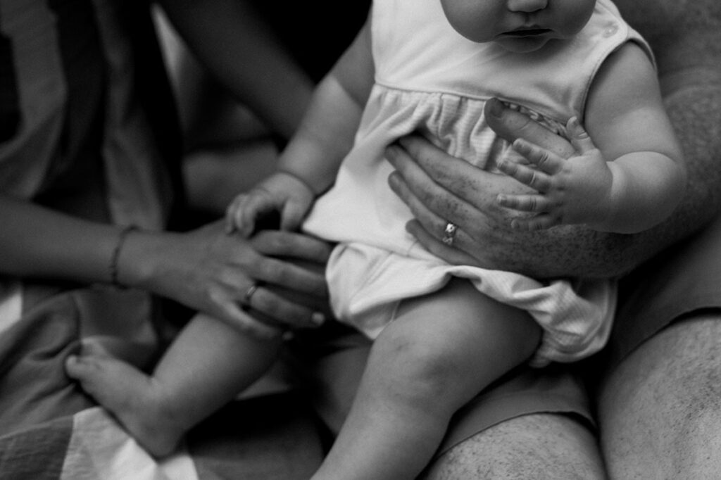 A family holds their baby close during Greenville SC Family Portraits at Furman University, surrounded by flowers. Dani Lacey Photographs.