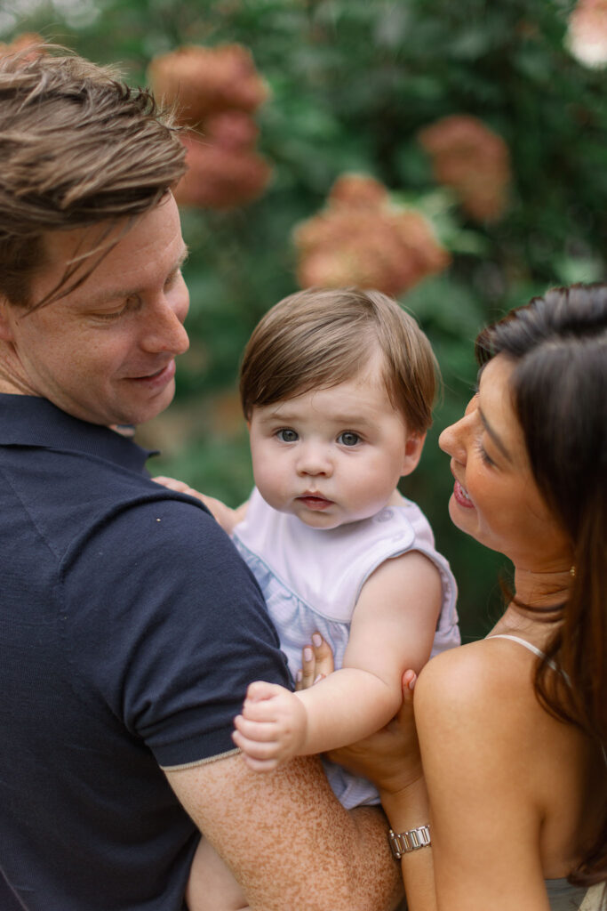 A family holds their baby close during Greenville SC Family Portraits at Furman University, surrounded by flowers. Dani Lacey Photographs.