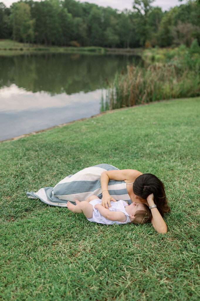 A mother and baby lying together on the grass by the lake during Greenville SC Family Portraits at Furman University. Dani Lacey Photographs.