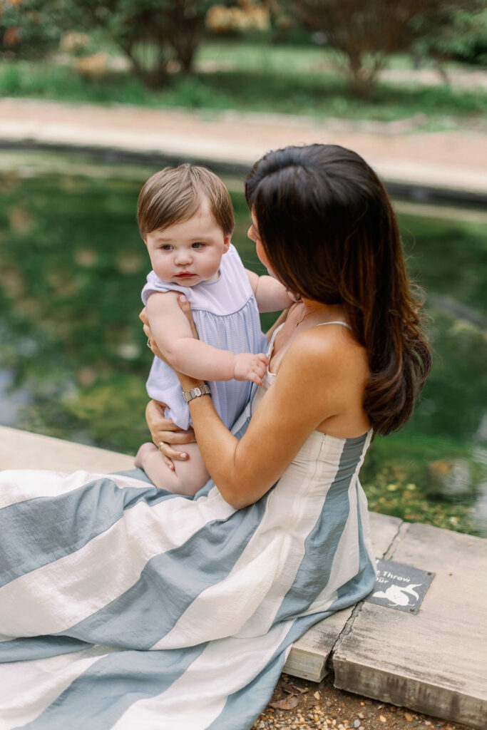 A mom holds her baby while sitting by the pond during Greenville SC Family Portraits at Furman University. Dani Lacey Photographs.