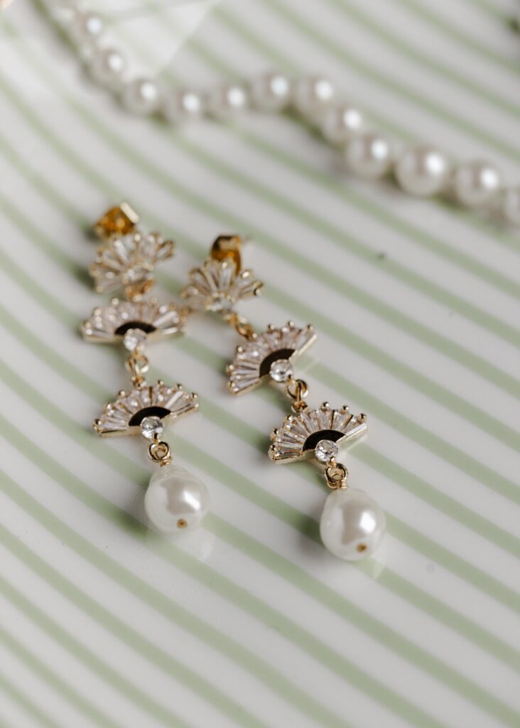 Elegant pearl and gold bridal earrings styled on a striped plate, photographed by Greenville wedding photographer Dani Lacey Photographs.