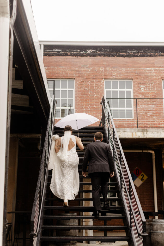 Bride and groom walking upstairs with an umbrella at Judson Mill wedding in Greenville SC, editorial wedding photography. Dani Lacey Photographs.