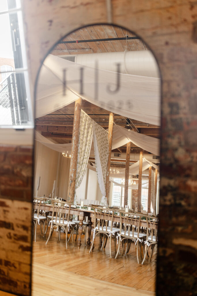 Wedding reception mirror signage with H + J monogram reflecting draped industrial reception space at Judson Mill. Dani Lacey Photographs.