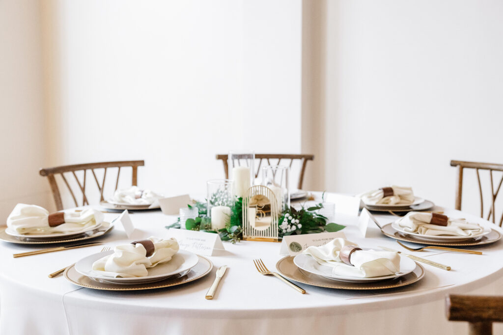 Round wedding reception table set with gold flatware, white napkins, candles, and greenery centerpiece at Judson Mill. Dani Lacey Photographs.