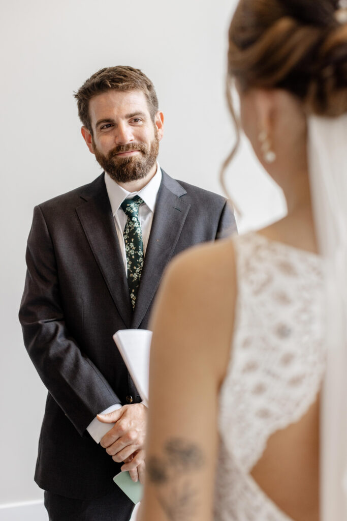 Groom smiles while listening to bride’s vows during their first look at Judson Mill in Greenville.