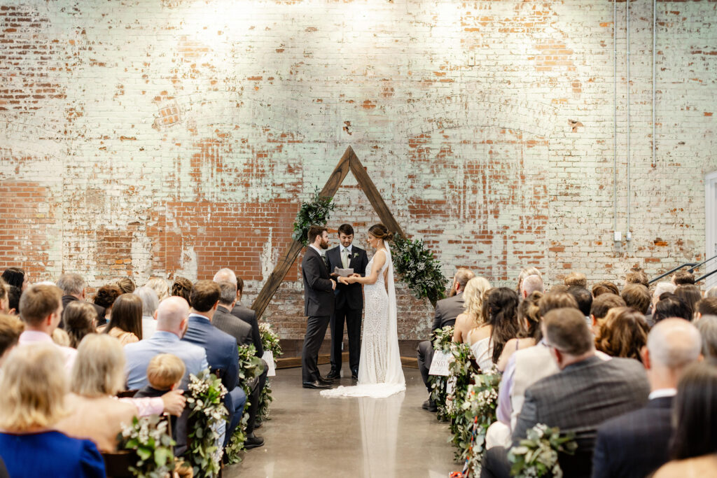 Wedding ceremony with rustic brick wall backdrop and wooden arch at Judson Mill Greenville | Dani Lacey Photographs