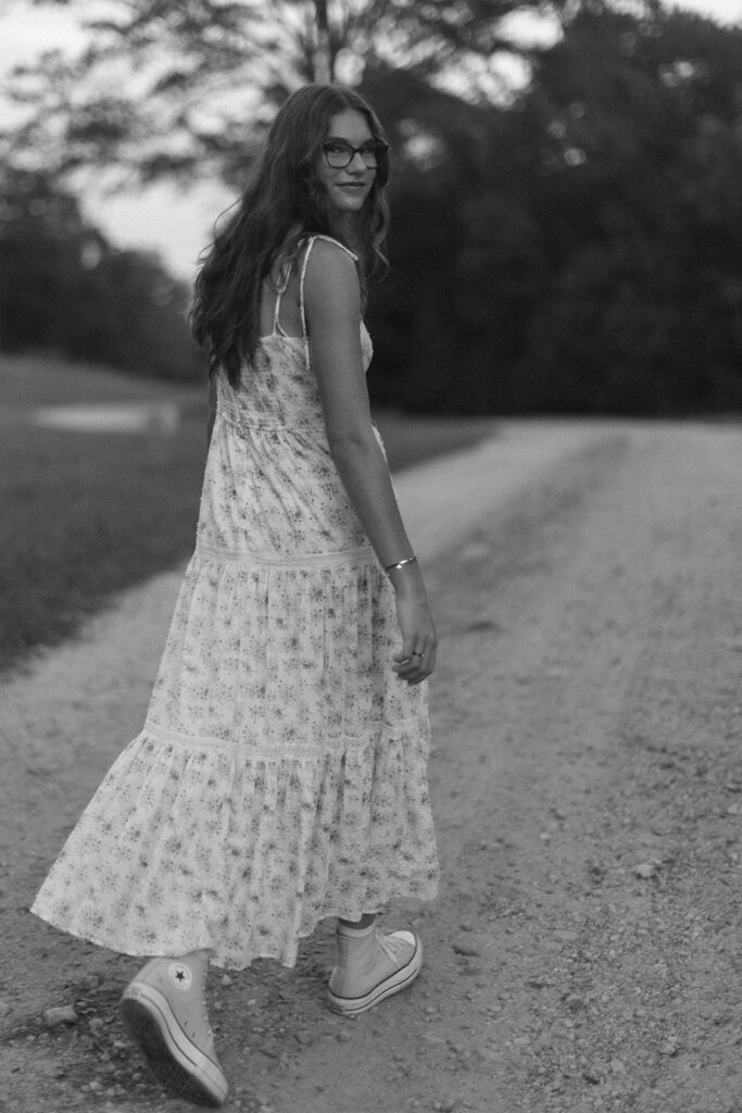 Teen girl walking down a dirt path in a floral dress during a black and white Greenville SC photo session. Dani Lacey Photographs.