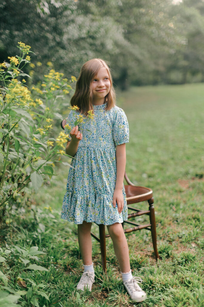 Young girl in floral dress holding yellow flowers during an at-home family session in Greenville SC. Dani Lacey Photographs.
